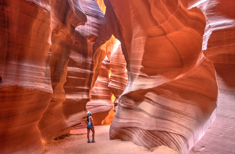 A woman standing in the mesmerizing Antelope Canyon, surrounded by wavy red walls.]