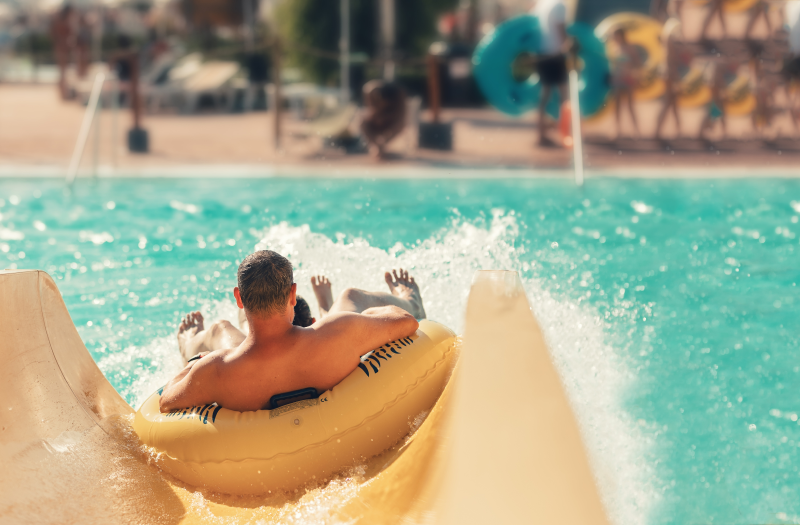 A man on a yellow inner tube sliding into crystal-clear water at a water park.