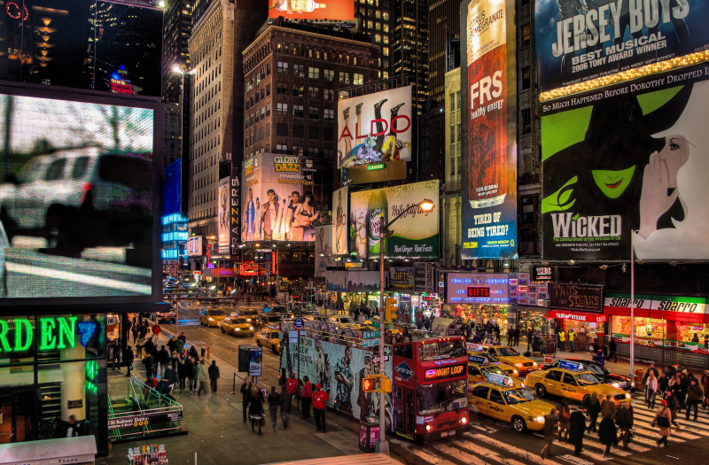A crowded evening in New York City’s Times Square with pedestrians, traffic, and a double-decker bus.